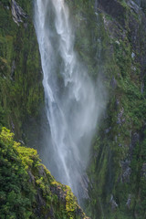 Detail of a portion of a misty waterfall falling down a moss-covered rock wall