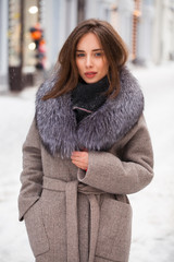 Young brunette woman in a gray coat with a fur collar