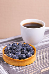 Tasty blueberry tartlet with vanilla cream and cup of coffee