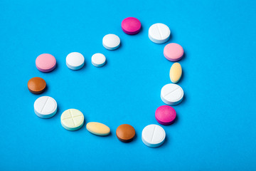 Conceptual background on the pharmaceutical theme on a blue background is lined with a heart from different multi-colored pills, close-up pills for cardiology.