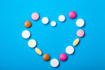 Symbol of love heart of multicolored tablets of round and oval shape close-up on a blue background top view.