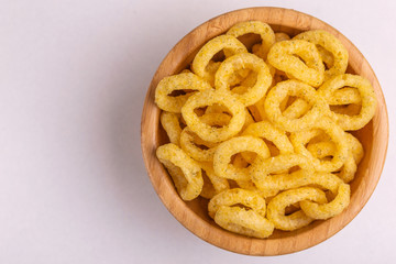 Puff corn rings in wooden bowl on light background