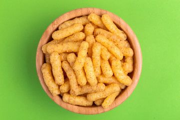 Crunchy corn sticks in wooden bowl on bright colored background
