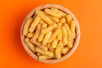 Crunchy corn sticks in wooden bowl on bright colored background