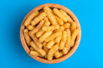 Crunchy corn sticks in wooden bowl on bright colored background