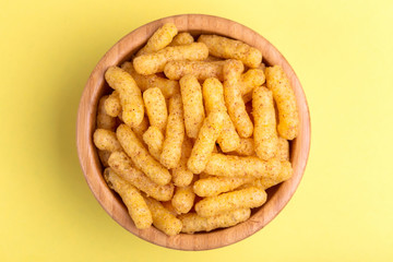 Crunchy corn sticks in wooden bowl on bright colored background