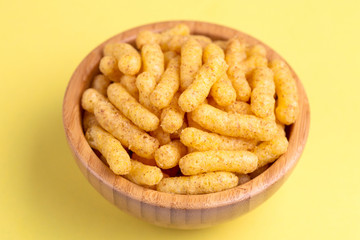 Crunchy corn sticks in wooden bowl on bright colored background