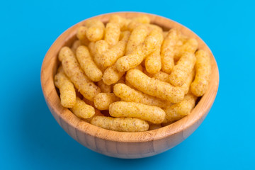 Crunchy corn sticks in wooden bowl on bright colored background