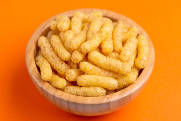 Crunchy corn sticks in wooden bowl on bright colored background