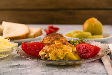 Meat casserole under cheese crust. Pickled vegetables. Red tomato slices. Close-up. Copy space.
