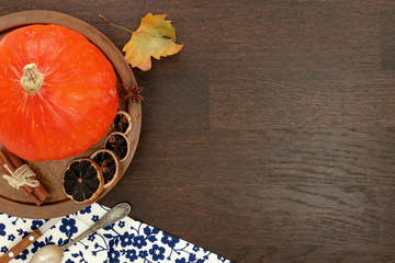Round orange pumpkin with autumn leaf and other objects, flat lay on wooden background.
