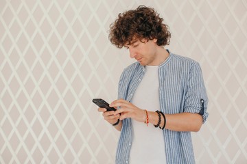 Curly brunet checking messages or typing something with his phone indoors