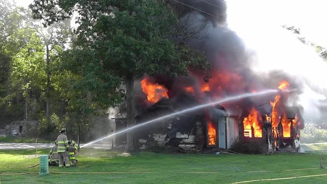 Firemen shooting a water hose towards a blazing house fire