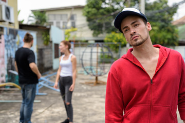 Young bearded man thinking while wearing cap with happy young co
