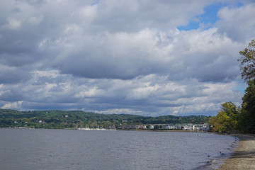 Fototapeta na wymiar Croton-On-Hudson, New York, USA: View of houses and a marina on the Hudson River under a cloud-filled sky, from a pebble beach in Croton Point Park.