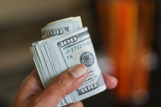 Hand holds roll of 100 dollar bills
