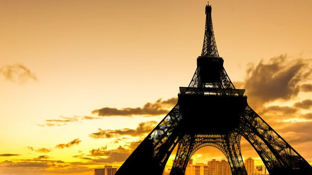 Tour Eiffel backlight and orange sky with moving clouds time lapse from sunset changing light to dark above cityscape of Paris in France.