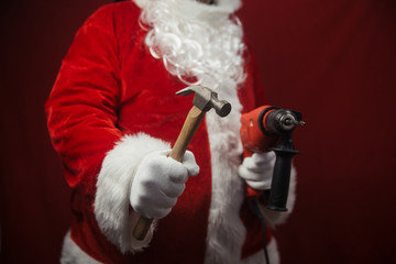 Santa Claus holding hammer and drill in hands busy preparing decoration. Closeup view of building...