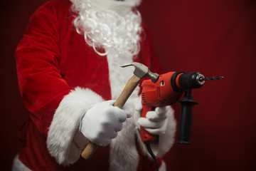Santa Claus holding hammer and drill in hands busy preparing decoration. Closeup view of building...