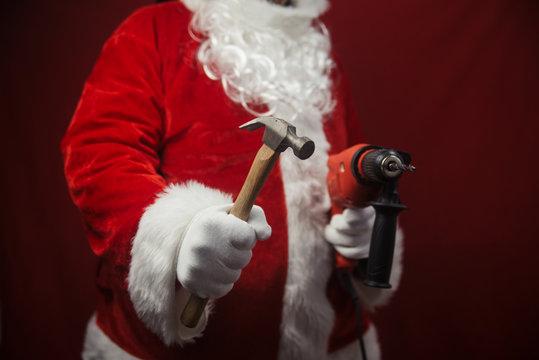 Santa Claus holding hammer and drill in hands busy preparing decoration. Closeup view of building creative ideas, taking job. Happy Christmas and New Year time renovation design background.