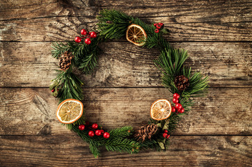 Christmas wreath of Fir branches, cones, red decoration on wooden background with snowflakes. Xmas and Happy New Year theme. Flat lay, top view
