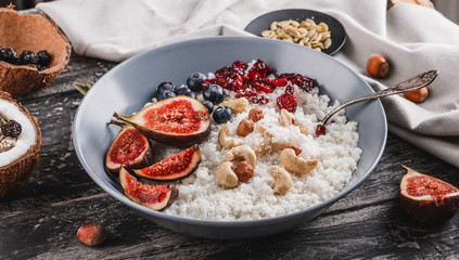 Rice coconut porridge with figs, berries, nuts, dried apricots and coconut milk in plate on rustic wooden background. Healthy breakfast ingredients. Clean eating, vegan food concept