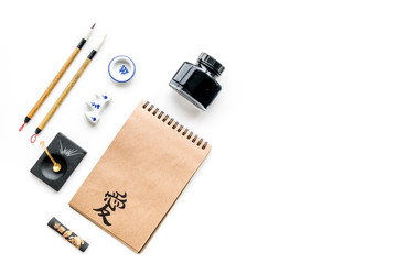Chinese or japanese calligraphy pattern. Hieroglyph love in craft paper notebook and writing accessories on white background top view space for text