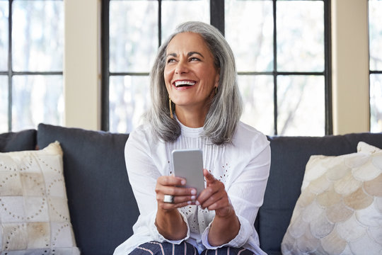 Mature woman with grey hair texting on cell phone in living room at home