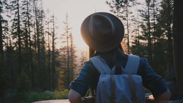 Back view excited female tourist with backpack enjoying amazing sunset with arms wide open at Yosemite park slow motion.