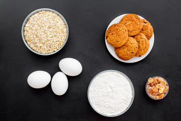 Ingredients for homemade cookies. Oatmeal cookies. Fresh cookies near flour, eggs, oatmeal, nuts and flour on black background top view