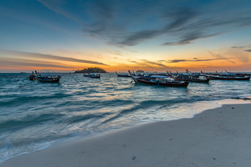 Silhouette of Traditional Thai fishing boats or long tail boats parking at the fishing boat bay at tropical sunrise.