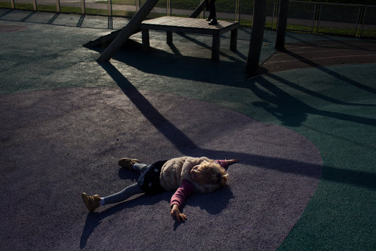 I don't want to go home! Little girl lying on the ground in a playground at dusk.