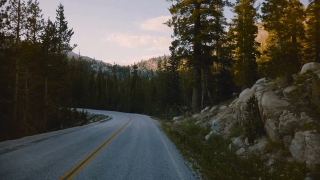 POV camera in car moving along beautiful forest mountain road between rocks on sunset in Yosemite park slow motion.