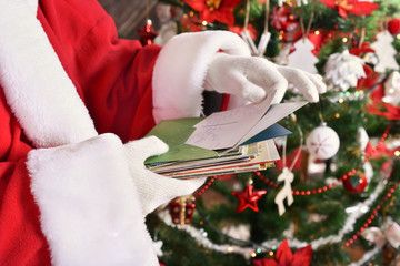 santa claus reading letters from children in front of christmas tree