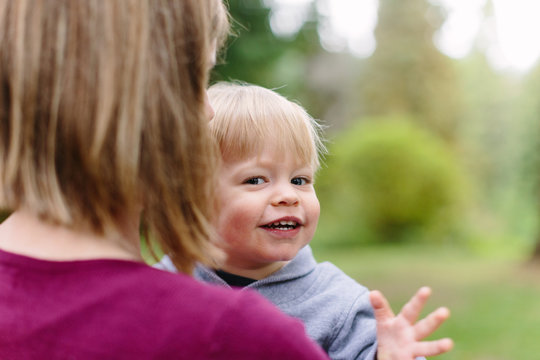 Happy Little Boy Looking over Mom's Shoulder and Waving