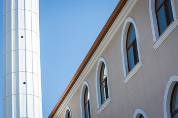 High rise building with semicircular windows next to white column against blue sky.