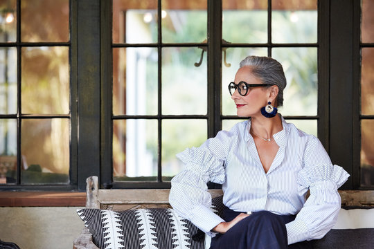 Portrait of beautiful and stylish mature woman interior designer with grey hair sitting on front porch