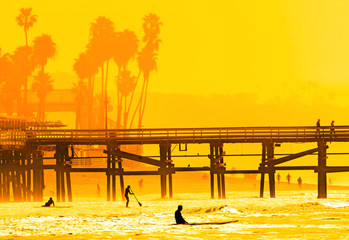 Surfers at San Clemente pier in the golden light of a summer sunset in Southern California - obrazy, fototapety, plakaty