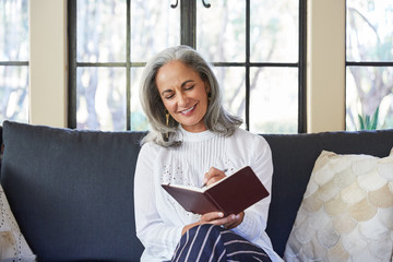 Mature woman with grey hair journaling in living room
