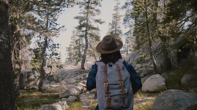 Camera follows young tourist girl hiking alone with backpack up on beautiful rocks at Yosemite national park slow motion