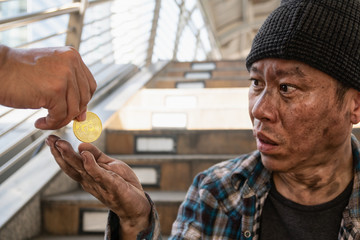 a man hand donate Bitcoin golden coin to Asian poor homeless beggar who look with surprise eyes