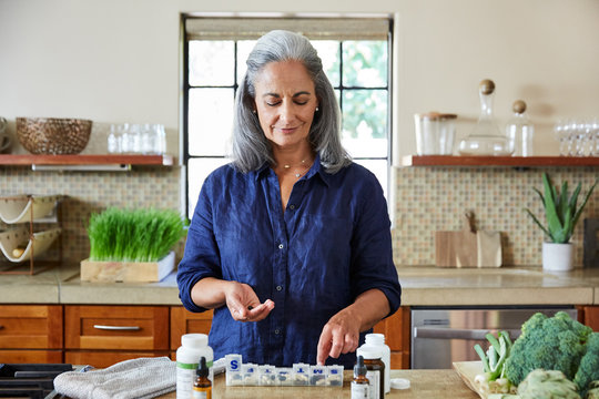 Mature woman organizing her health supplements  in the kitchen 
