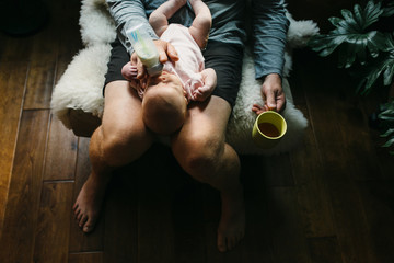 Dad bottle feeding newborn baby girl on chair at home