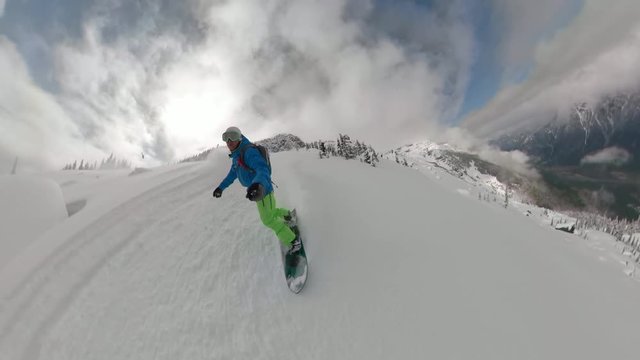 VR360: Snowy wilderness surrounding snowboarder carving down the breathtaking mountain in British Columbia. Man on awesome winter vacation shredding fresh snow while speeding down a steep hill.