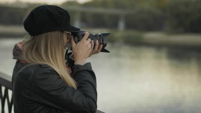 Professional young blonde woman photographer with digital camera taking pictures of autumn river at evening city city. Close Up, shallow depth of field.