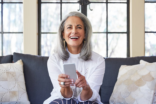 Mature woman with grey hair texting on cell phone in living room at home