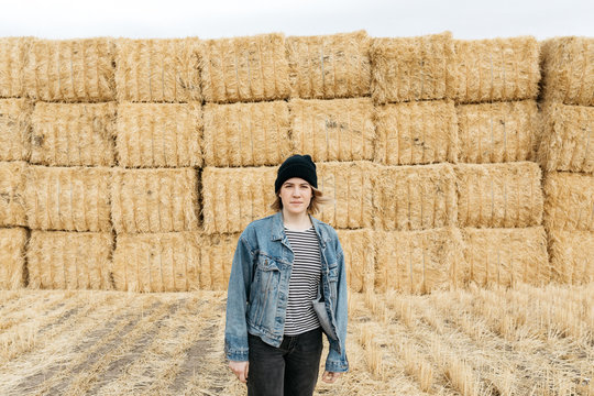 Lifestyle portrait of young adult female wearing denim coat in hay field after harvest