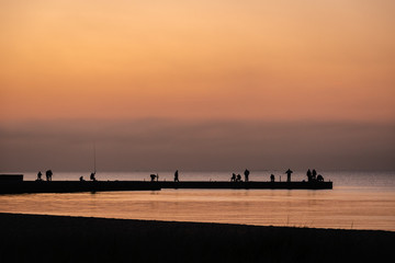 Silhouette of people fisherman on pier while beautiful sea sunset or dawn