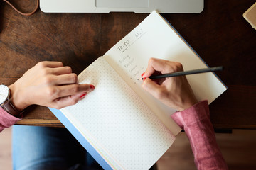 Top view of woman's hands writing to-do's list in notebook.