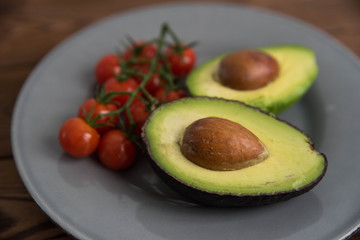 Healthy fresh avocado and cherry tomatoes on the plate on brown wooden background